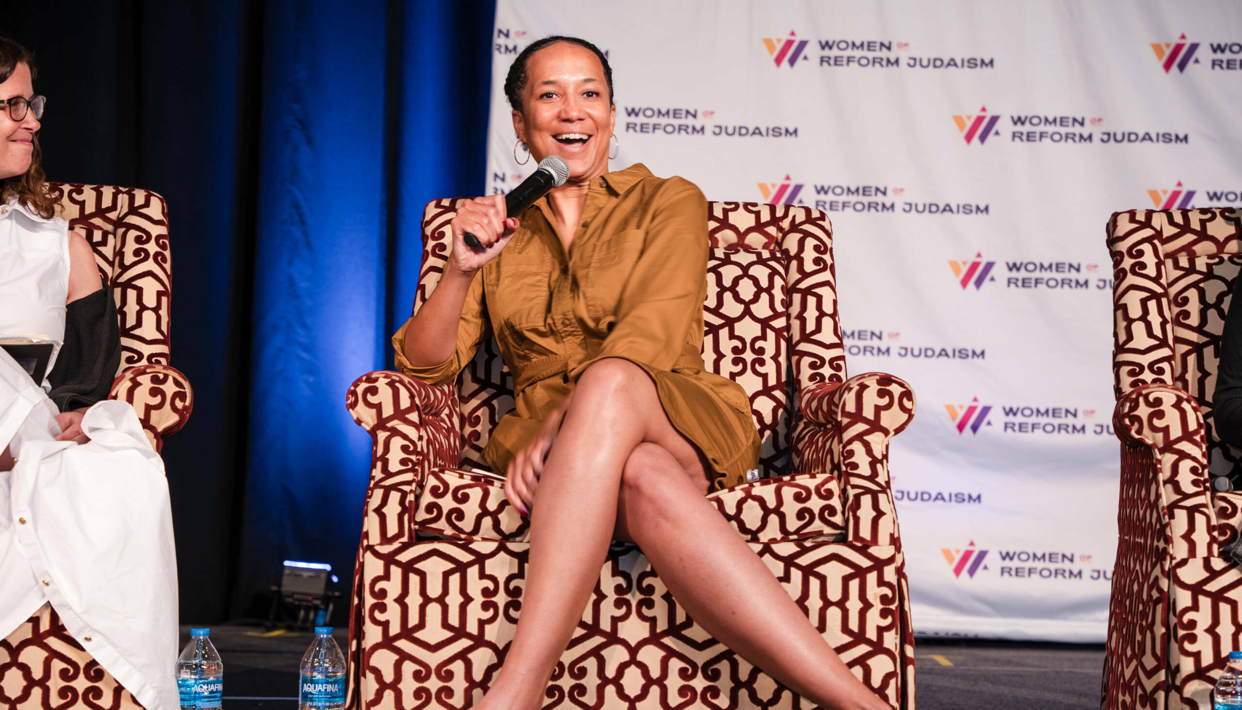 A woman sitting in a patterned chair speaking into a microphone