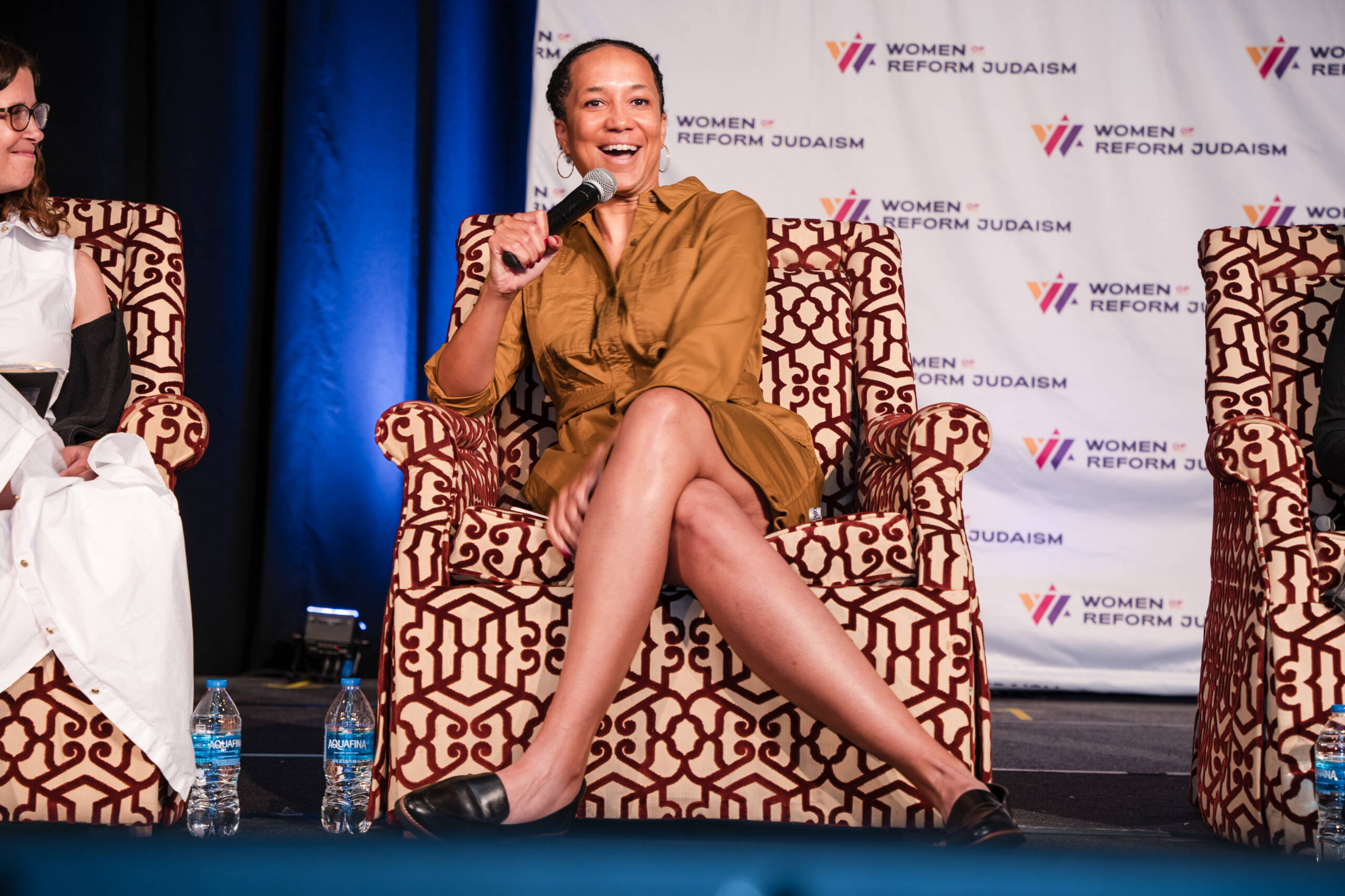 A woman sitting in a patterned chair speaking into a microphone